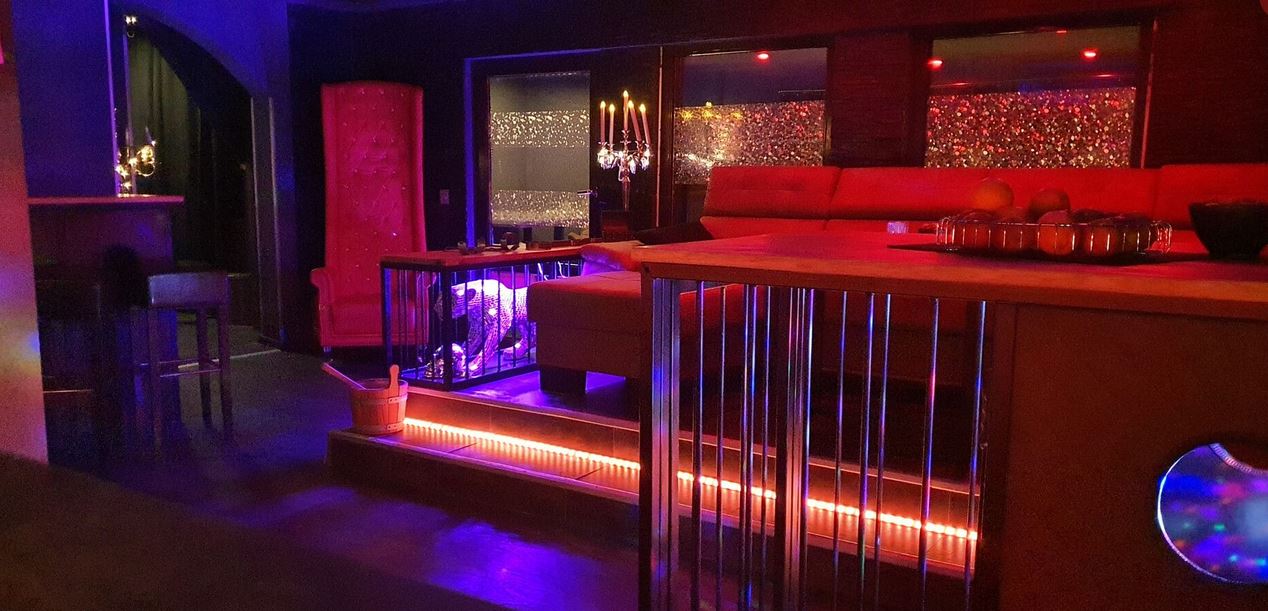 Bar Lounge des Club TraumPalais mit Theke, Hockern und roter Sitzecke.