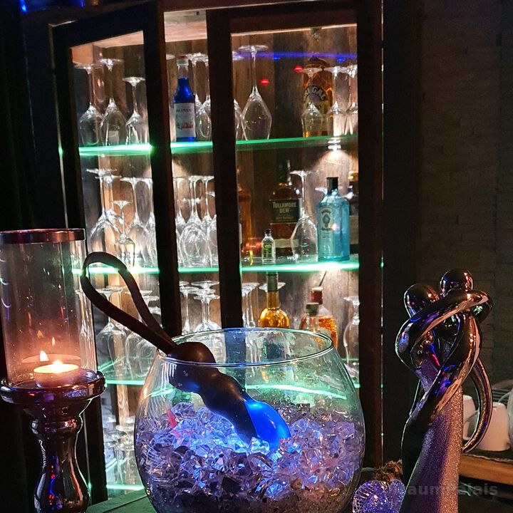 Bar mit beleuchtetem Glasregal, Gläsern und Flaschen.